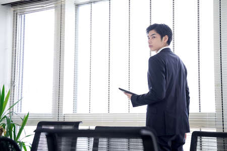 Japanese male businessman with a tablet by the window of the officeの写真素材