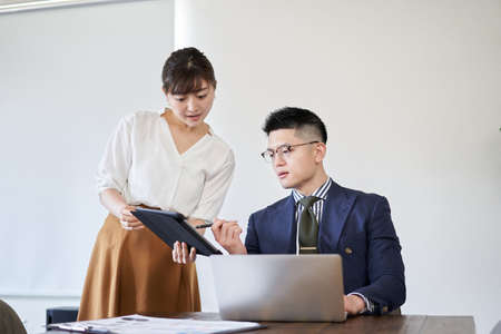Businesswoman asking senior Asian businessman to check materials