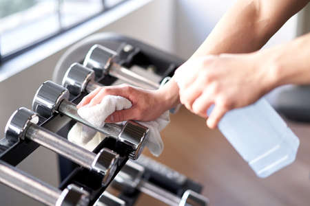 Asian male trainer to disinfect dumbbells at training gym