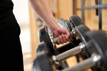 Asian man taking dumbbell from rack