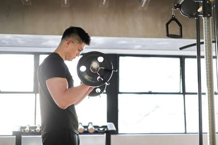 Asian man in barbell curls at training gym