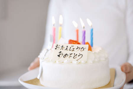 Asian mom carrying a cake that says Happy Birthday in Japaneseの写真素材