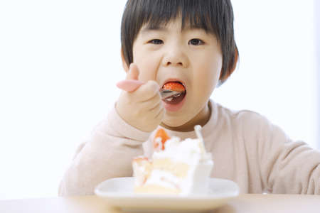 Asian boy eating birthday cake with a smileの写真素材