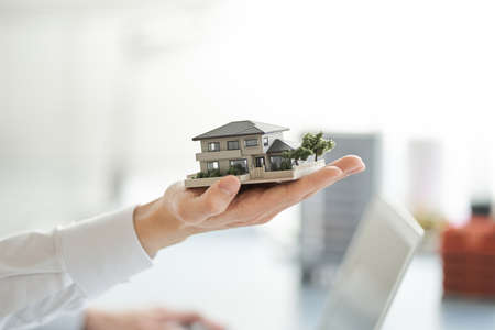 Hands of an Asian man holding an architectural model of a single houseの写真素材