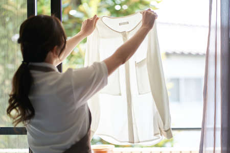 Asian woman hanging laundry by the windowの写真素材