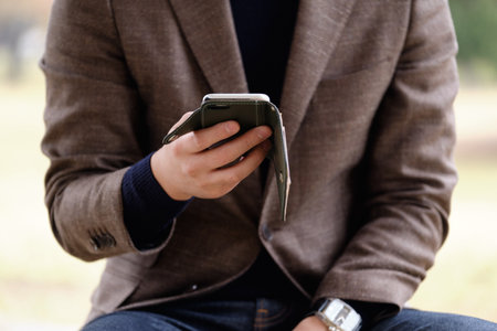 A man wearing a jacket operating a smartphone outdoorsの写真素材
