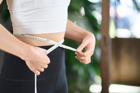 Asian woman measuring her waist size with a tape measure