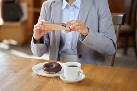 Asian woman taking a photo using a smartphone at a cafeの写真素材
