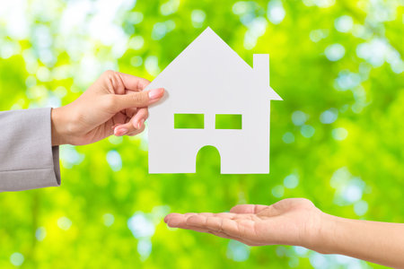 A woman's hand passing a white paper in the shape of a houseの写真素材