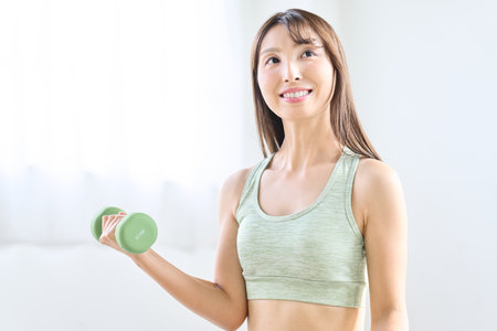 Asian woman doing dumbbell training at homeの写真素材