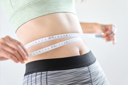 A woman measuring her stomach circumference with a tape measureの写真素材
