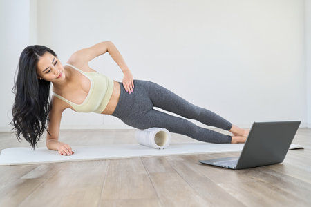A woman using a foam roller while watching a videoの写真素材