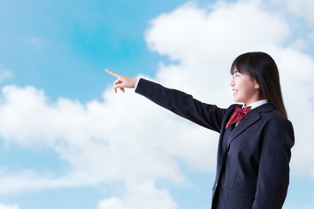 Female student pointing under the blue skyの写真素材
