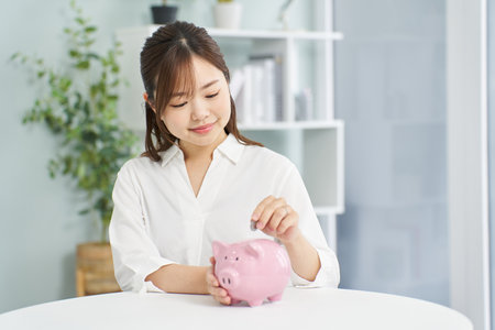 A woman putting money into a pig piggy bankの写真素材