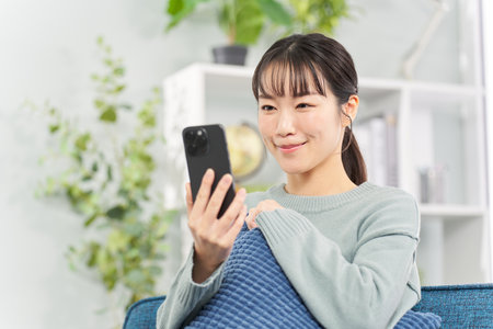 Woman sitting on sofa and looking at smartphoneの写真素材