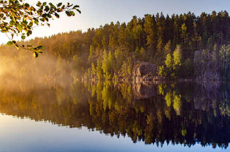 summer setting sun illuminating the rocks over a calm lakeの写真素材