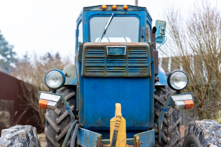 A front photo of an old blue tractor with fence and trees on backgroundの写真素材