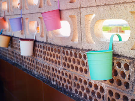 several multi-colored pots hanging on a brick wall at sunny day