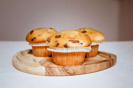 Three delicious muffins with chocolate peices on a wooden tray on a white tableの写真素材