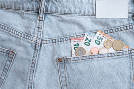 several euro banknotes and coins in the back pocket of light blue jeans.