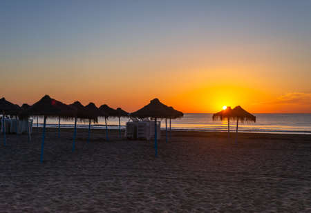 scenic view of the sea beach with reed sun umbrellas at sunriseの写真素材