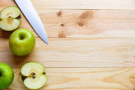 Flat lay photo of a few green apples and a knife on a natural wooden background.