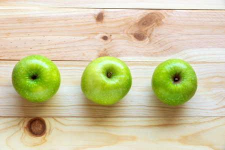 Flat lay photo of a three green, ripe and delicious apples on a natural wood backgroundの写真素材