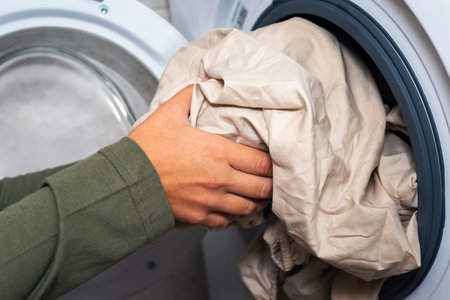 Human hand puts the laundry into the washing machine. house hold concept. Focus on a hand.の写真素材