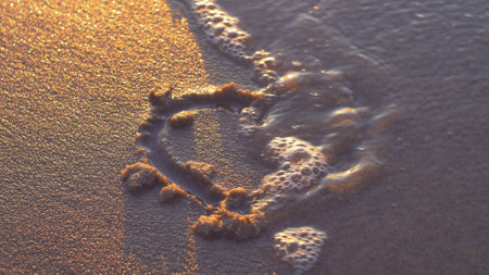 Heart Shapes Being Drawn on Sandy Beach and Wiped Out by Sea Wave at Sunsetの写真素材