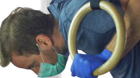 Man in Surgical Mask Works Out on Gymnastics Rings at Virus Epidemic Quarantineの写真素材