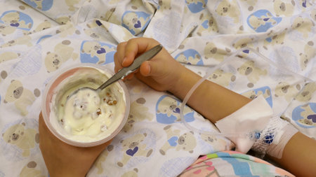 Young Girl on a Drip with Peripheral Venous Catheter Eating Meal in a Hospitalの写真素材