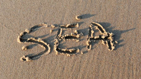 Sea Word Written on Sandy Beach and Wiped Out by Sea Wave at Sunsetの写真素材
