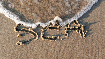 Sea Word Written on Sandy Beach and Wiped Out by Sea Wave at Sunsetの写真素材