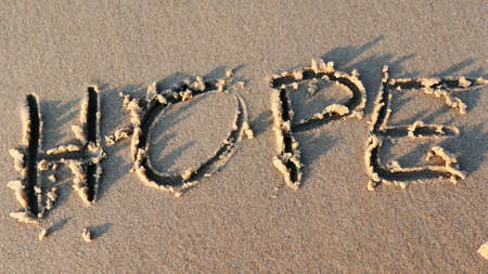 Hope Word Written on Sandy Beach and Wiped Out by Sea Wave at Sunsetの写真素材