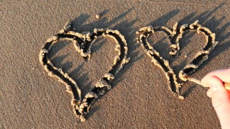 Drawing Heart Shape on Sandy Beach at Sunsetの写真素材