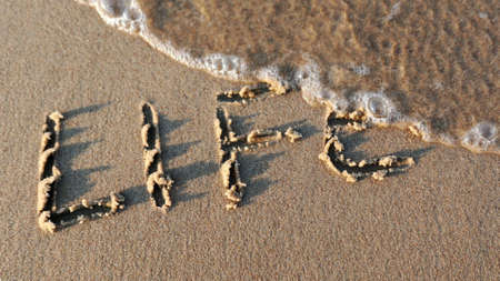 Life Word Written on Sandy Beach and Wiped Out by Sea Wave at Sunsetの写真素材