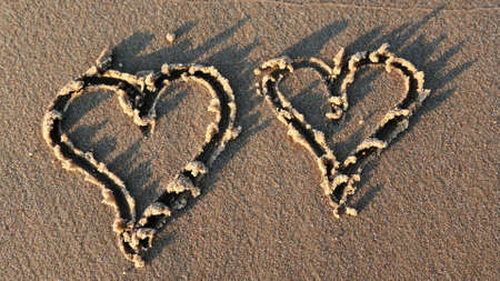 Drawing Heart Shape on Sandy Beach at Sunsetの写真素材