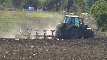 Farmer Ploughing Soil using Tractor with Mouldboard Plough on Sunny Dayの写真素材