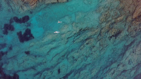 Aerial of People Swimming in Turquoise Sea at Rocky Coastlineの写真素材