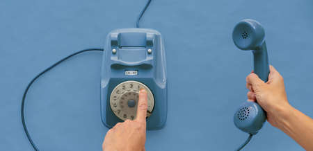 A blue vintage dial telephone handset with one hand and blue background.の写真素材
