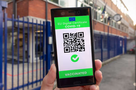 Woman showing on smartphone EU Digital Covid Certificate Green Pass with quad code. School background.の写真素材