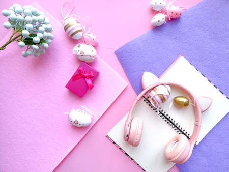 Easter flat lay composition. Pastel pink background with pastel purple and lilac flowers, gift box, pink headphones and notebook.の写真素材