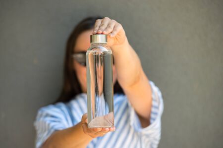 woman is holding and drinking from glass reusable bottle with clear water