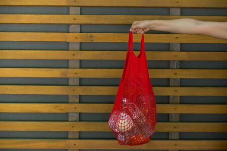 woman is holding mesh bag with products withoiy plastic package in front of wall with cioy spaceの写真素材