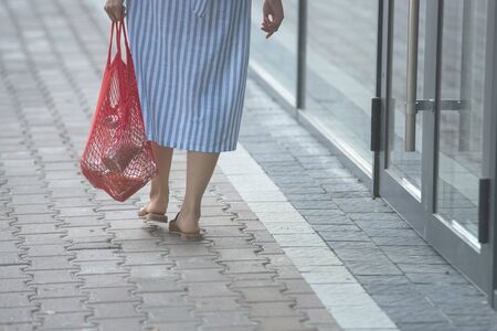 men is walking with mesh bag full of products withoiy plastic package in front of wall with cioy spaceの写真素材