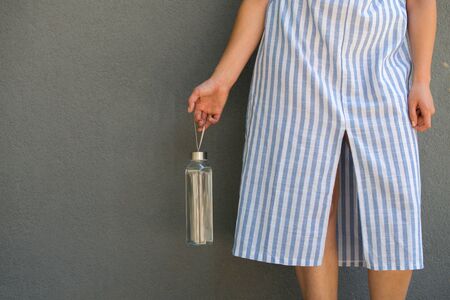 woman is holding and drinking from glass reusable bottle with clear waterの写真素材
