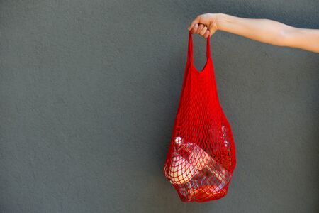 woman is holding mesh bag with products withoiy plastic package in front of wall with cioy space