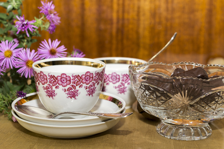 cups and chocolate in a crystal vase on a wooden table near a polished surfaceの写真素材