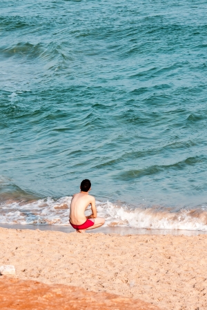 Young man sitting on the beach enjoying peaceful momentの写真素材
