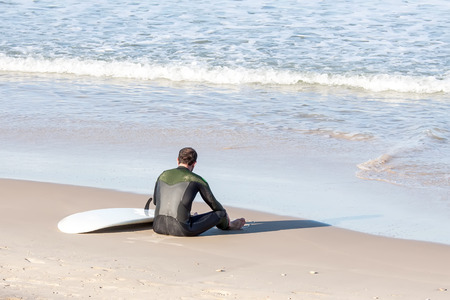 surfer sitting in the beach and checking the wavesの写真素材